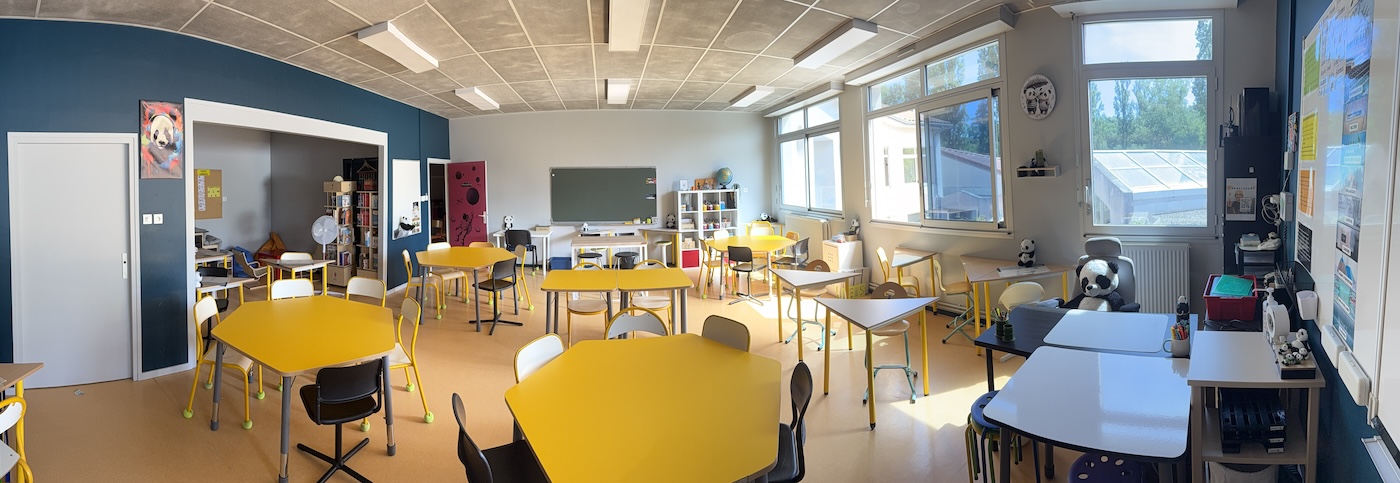 La classe modulable en rentrée 2026, vue panoramique : îlots jaunes, atelier ouvert sur le côté, coins de travail variés et grandes fenêtres donnant sur la serre.